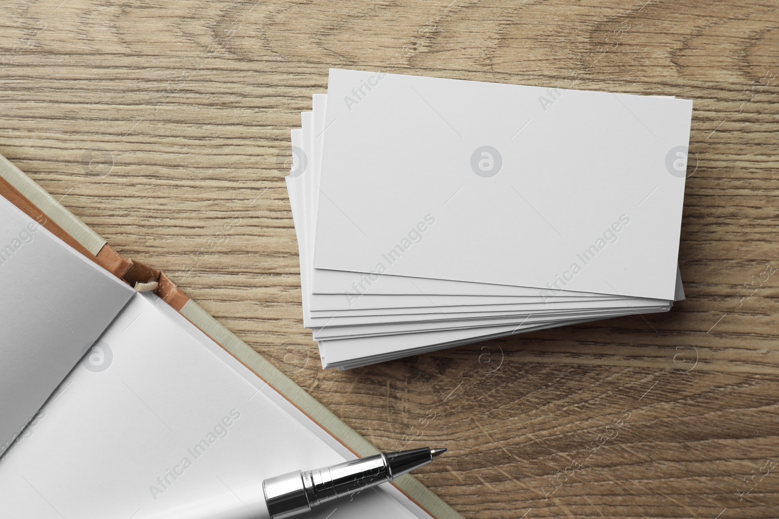 Photo of Stack of blank business cards, notebook and pen on wooden table, flat lay. Mockup for design