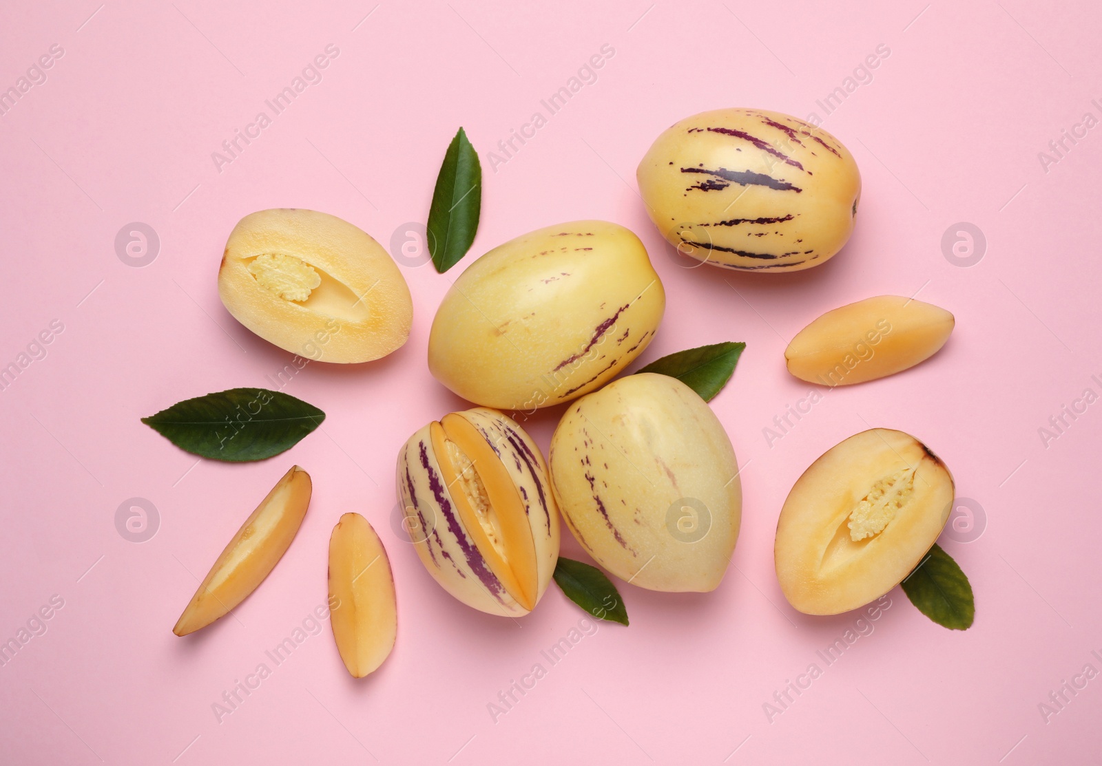Photo of Whole and cut pepino melons with green leaves on pink background, flat lay