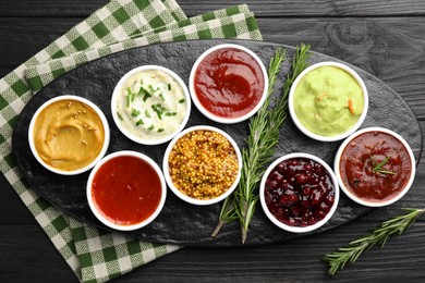 Different tasty sauces in bowls and rosemary on black wooden table, top view