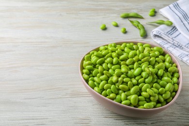 Photo of Bowl of delicious edamame beans on light wooden table, space for text