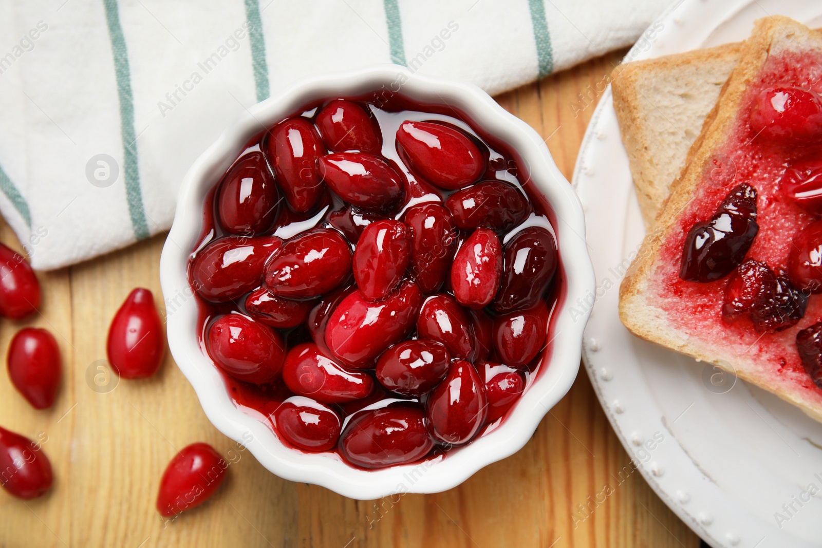 Photo of Delicious dogwood jam with berries and bread on wooden table, flat lay