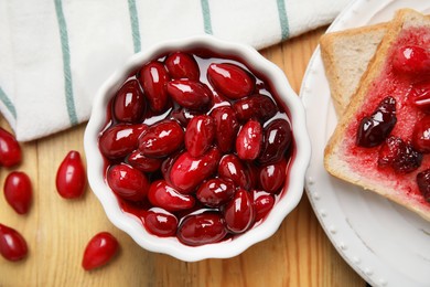 Photo of Delicious dogwood jam with berries and bread on wooden table, flat lay