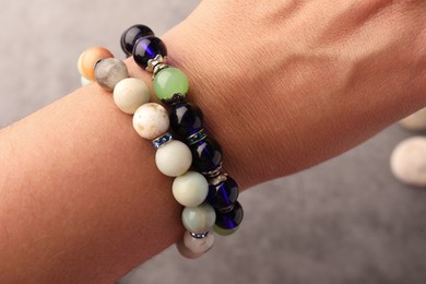 Photo of Woman wearing beautiful bracelets with gemstones on blurred background, closeup