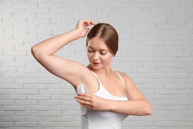 Photo of Young woman applying crystal alum deodorant to armpit against brick wall