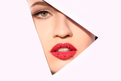 Photo of View of beautiful young woman with creative lips makeup through cutout in color paper