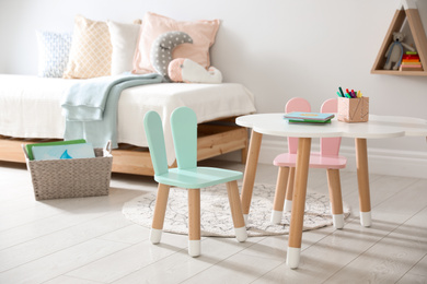 Photo of Small table and chairs with bunny ears in children's room interior