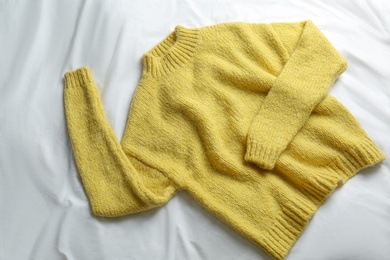 Photo of Stylish knitted sweater on white fabric, top view
