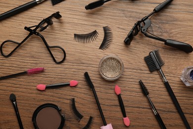 Flat lay composition with eyelash curlers, makeup products and accessories on wooden table