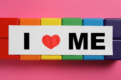 Sheet of paper with phrase I Love Me and colorful cubes on pink background, flat lay