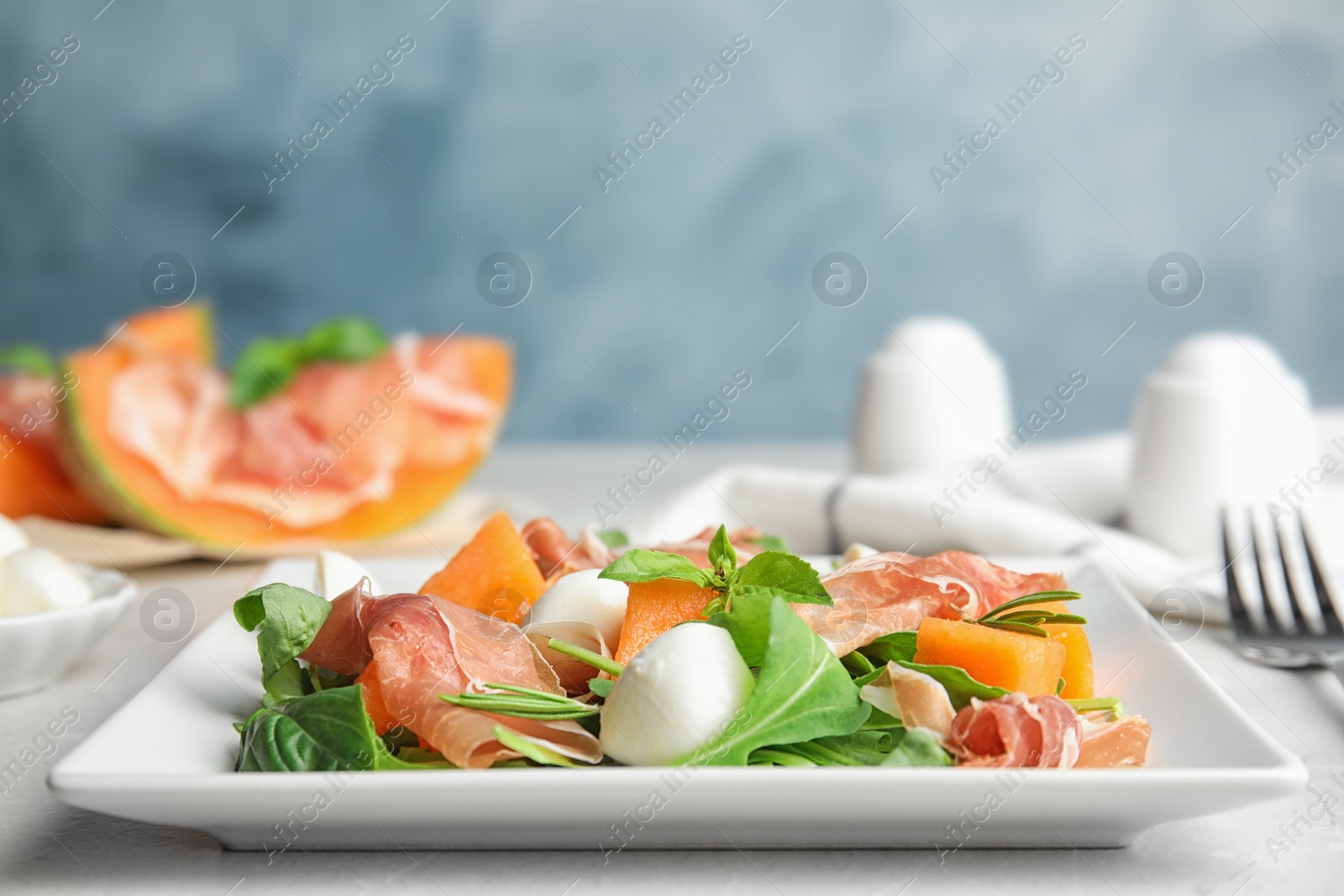 Photo of Fresh melon with prosciutto, mozzarella and arugula on table