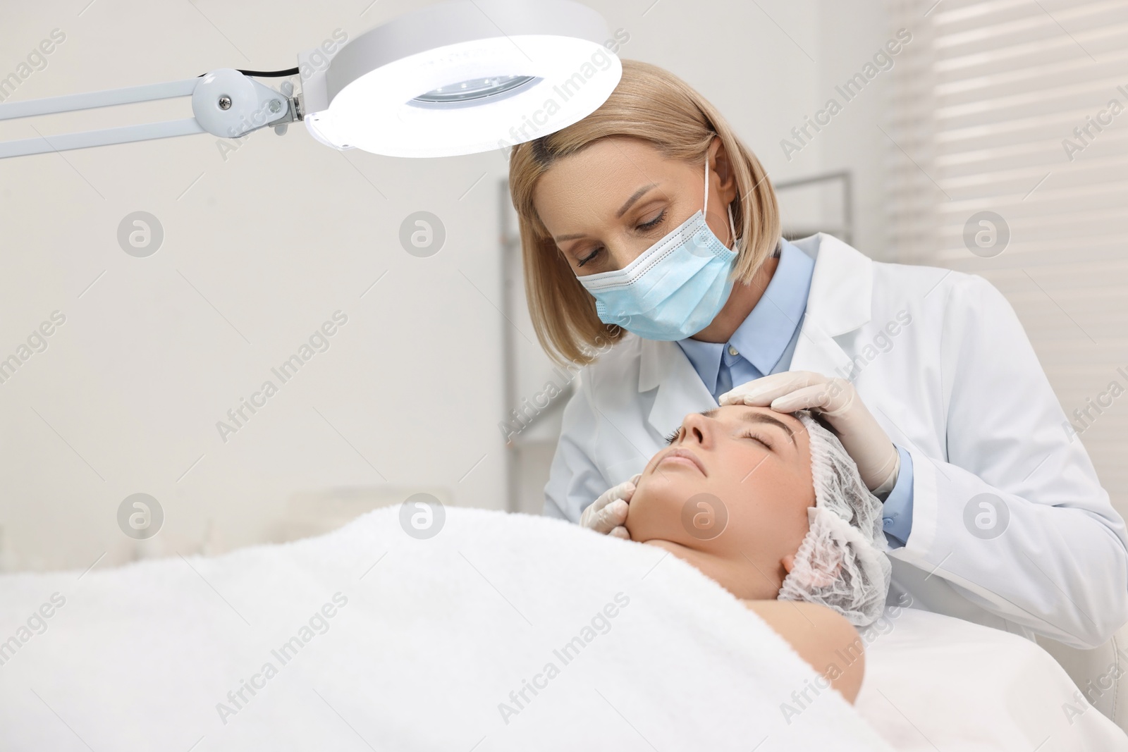 Photo of Dermatologist examining patient`s face under lamp in clinic