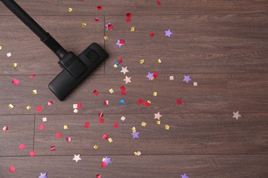 Photo of Vacuuming confetti from wooden floor, top view. Space for text