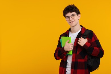 Photo of Portrait of student with backpack, notebooks and glasses on orange background. Space for text
