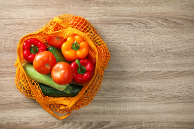 Photo of Net bag with vegetables on wooden table, top view. Space for text