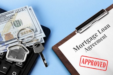 Image of Mortgage loan agreement with Approved stamp, house key, money and calculator on light blue background, closeup