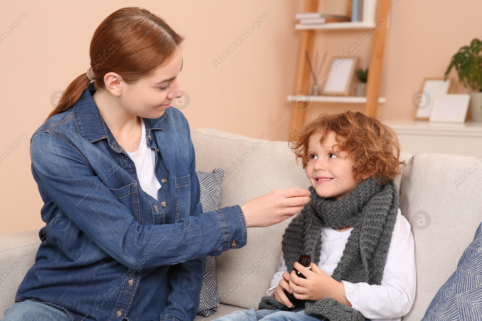 Photo of Mother giving cough syrup to her son on sofa at home