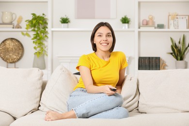 Happy woman watching TV on sofa at home