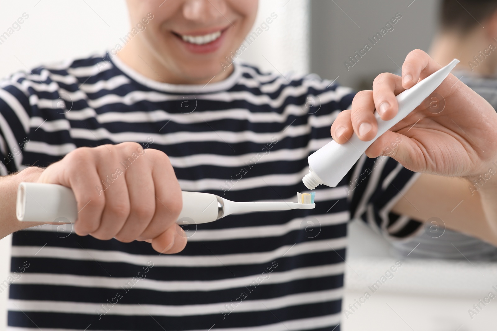 Photo of Man squeezing toothpaste from tube onto electric toothbrush in bathroom, closeup