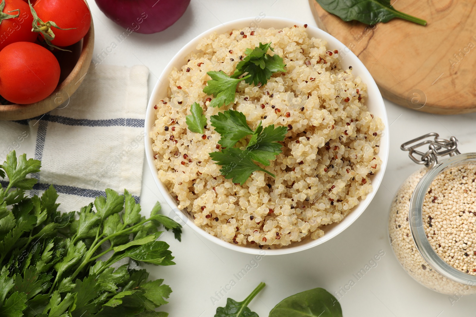 Photo of Tasty quinoa porridge with parsley in bowl on white marble table, flat lay