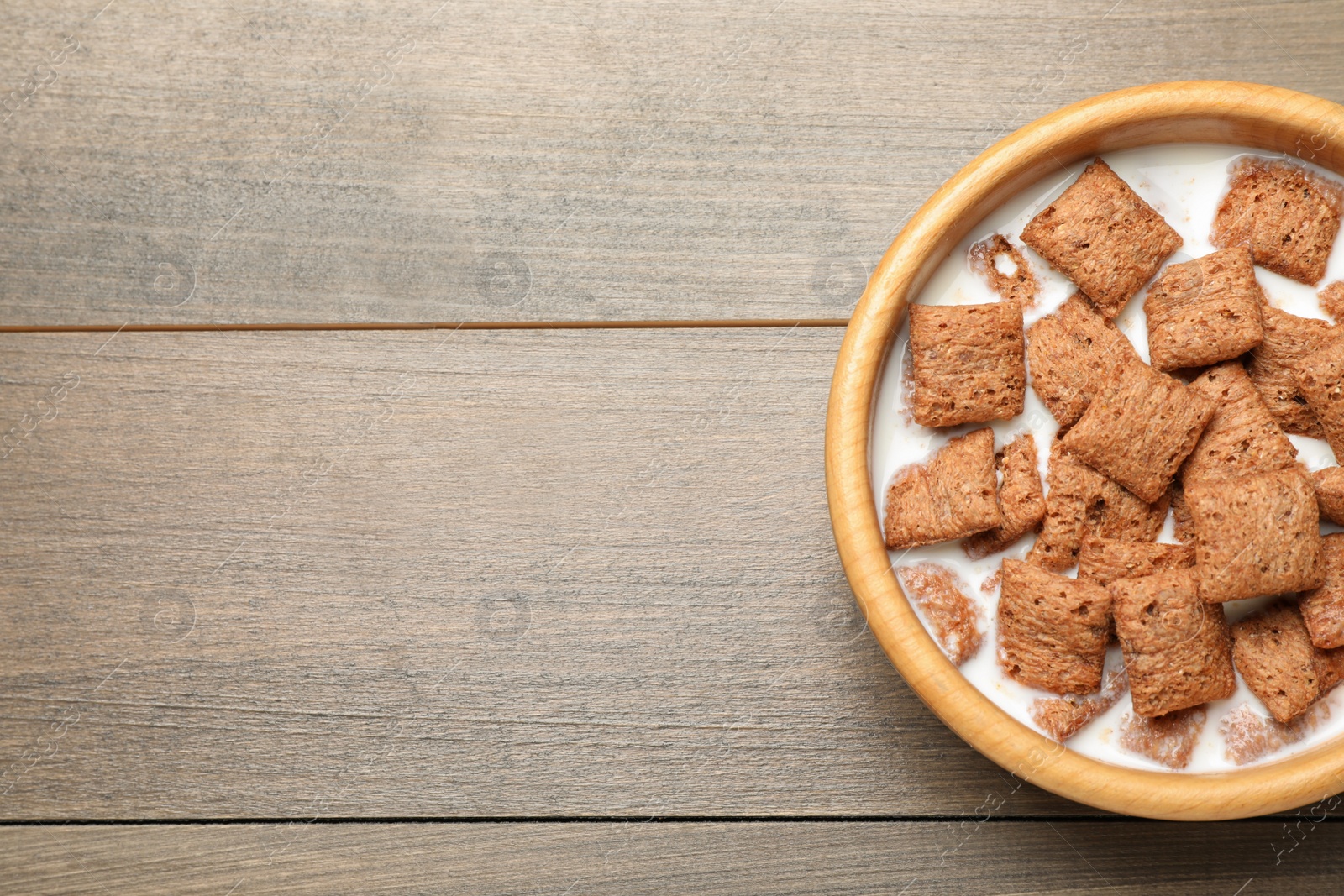 Photo of Tasty corn pads with milk in bowl on wooden table, top view. Space for text