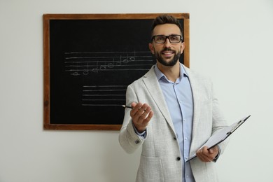 Teacher near black chalkboard with music notes in classroom