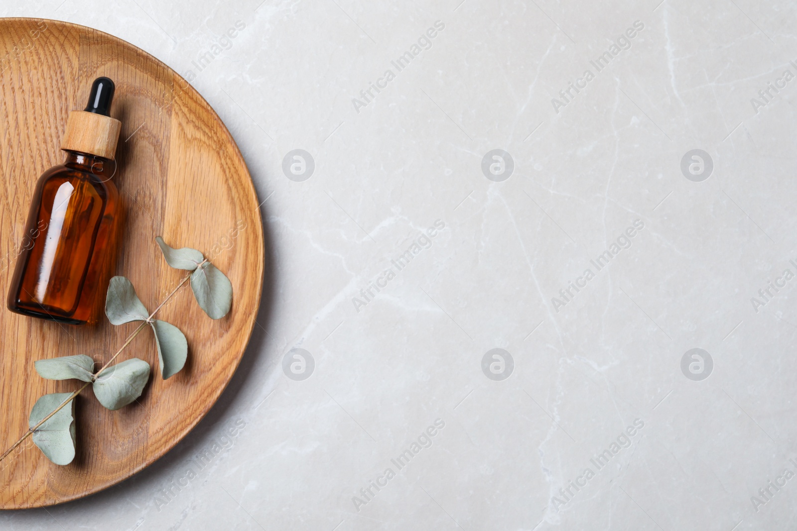 Photo of Wooden tray with bottle of face serum and leaves on grey marble table, top view. Space for text