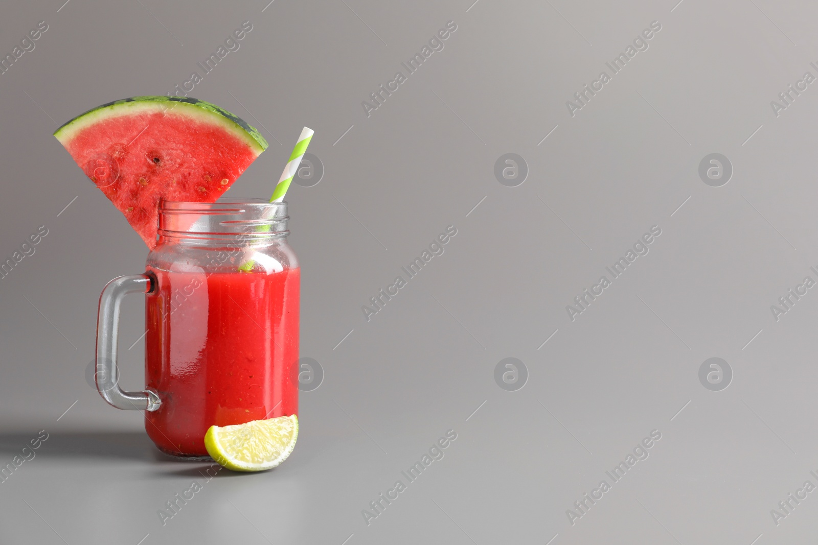 Photo of Tasty summer watermelon drink with lime in glass mason jar on grey background. Space for text