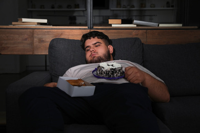 Photo of Depressed overweight man with sweets in living room at night