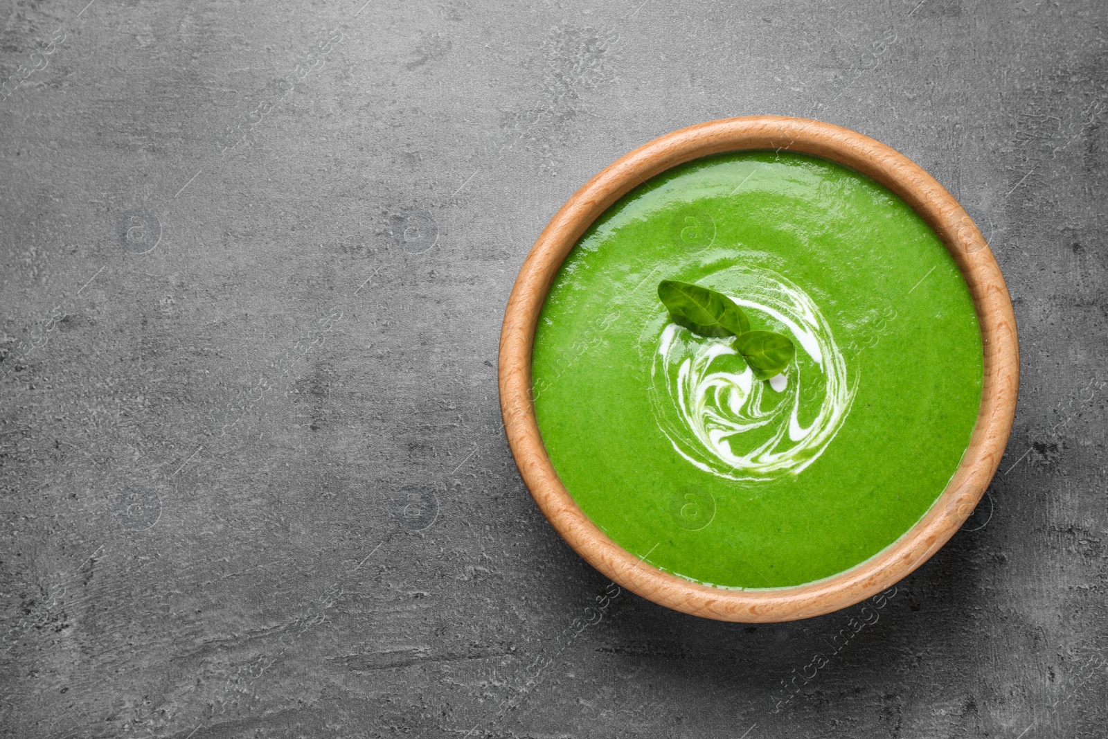 Photo of Bowl of healthy green soup with fresh spinach on grey table, top view. Space for text