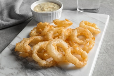 Closeup view of delicious golden breaded and deep fried crispy onion rings on marble board