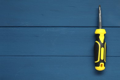 Screwdriver with bright handle on blue wooden table, top view. Space for text