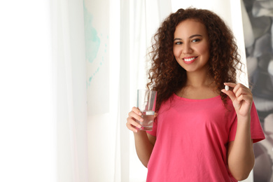 African-American woman with glass of water and vitamin pill indoors. Space for text