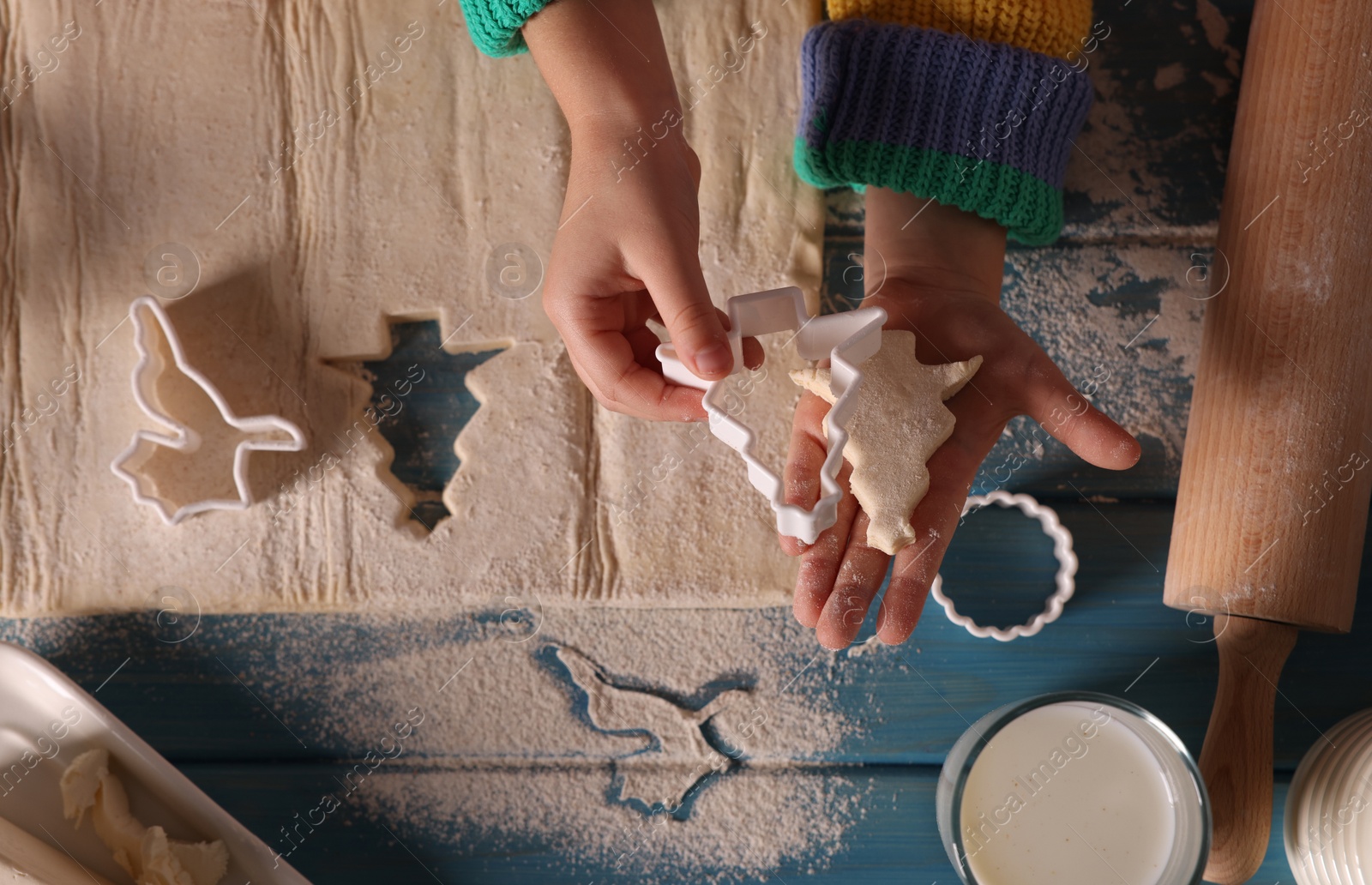 Photo of Little child making Christmas cookies at blue wooden table, top view