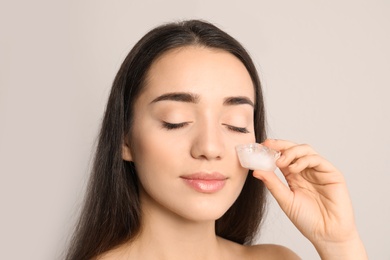 Young woman with ice cube on light background. Skin care