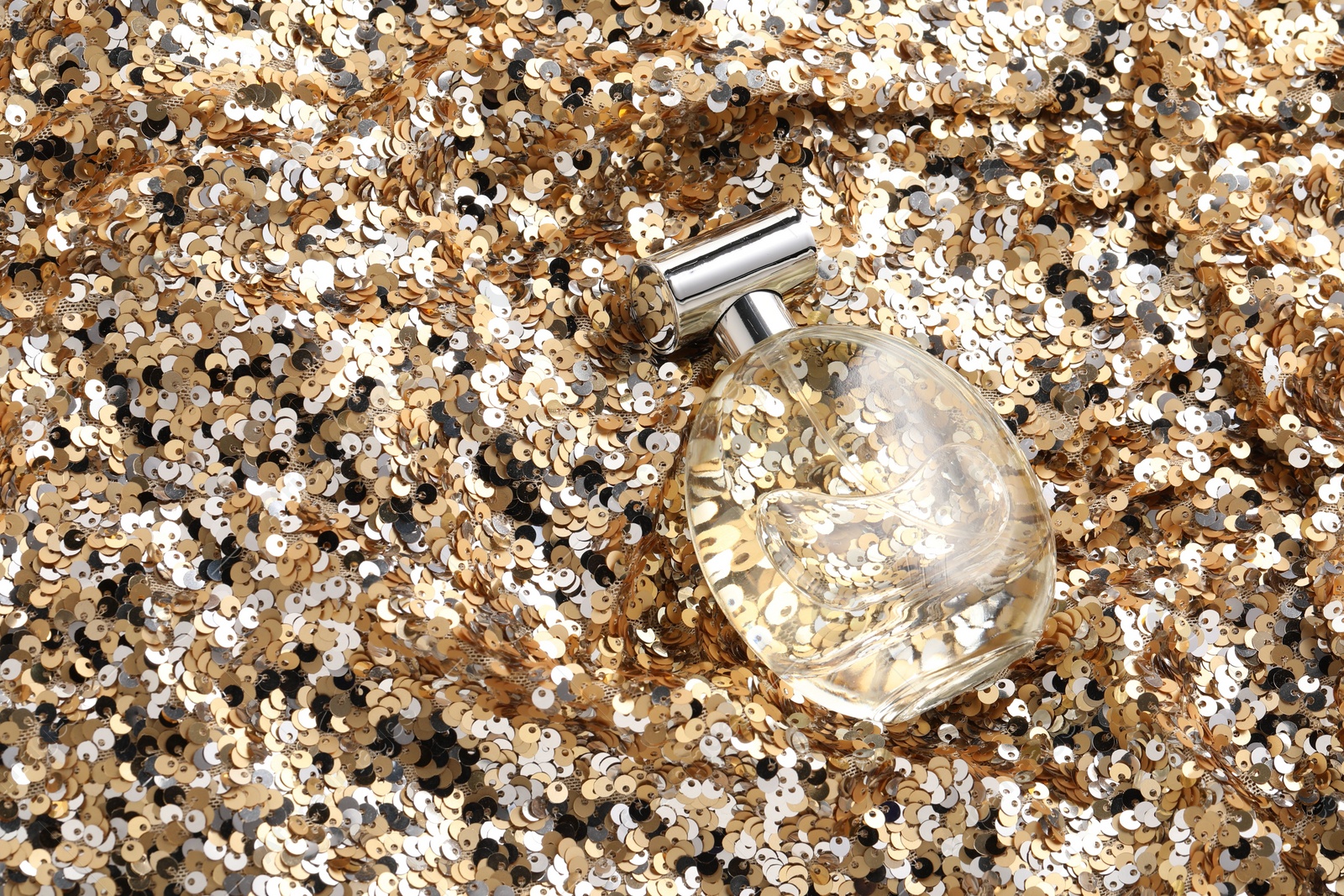 Photo of Luxury perfume in bottle on fabric with golden sequins, above view