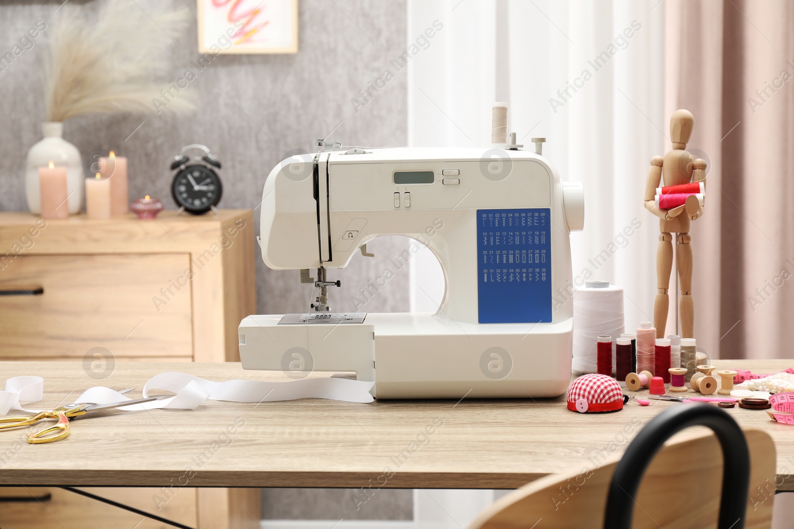 Photo of White sewing machine, cloth, craft accessories and mannequin on wooden table indoors