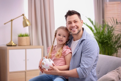 Father and daughter with piggy bank at home