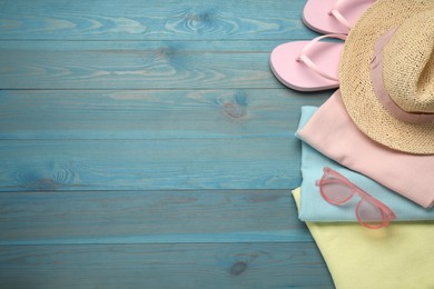 Beach towel, straw hat, flip flops and sunglasses on light blue wooden background, flat lay. Space for text