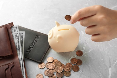Photo of Woman putting coin into piggy bank on grey stone table, closeup