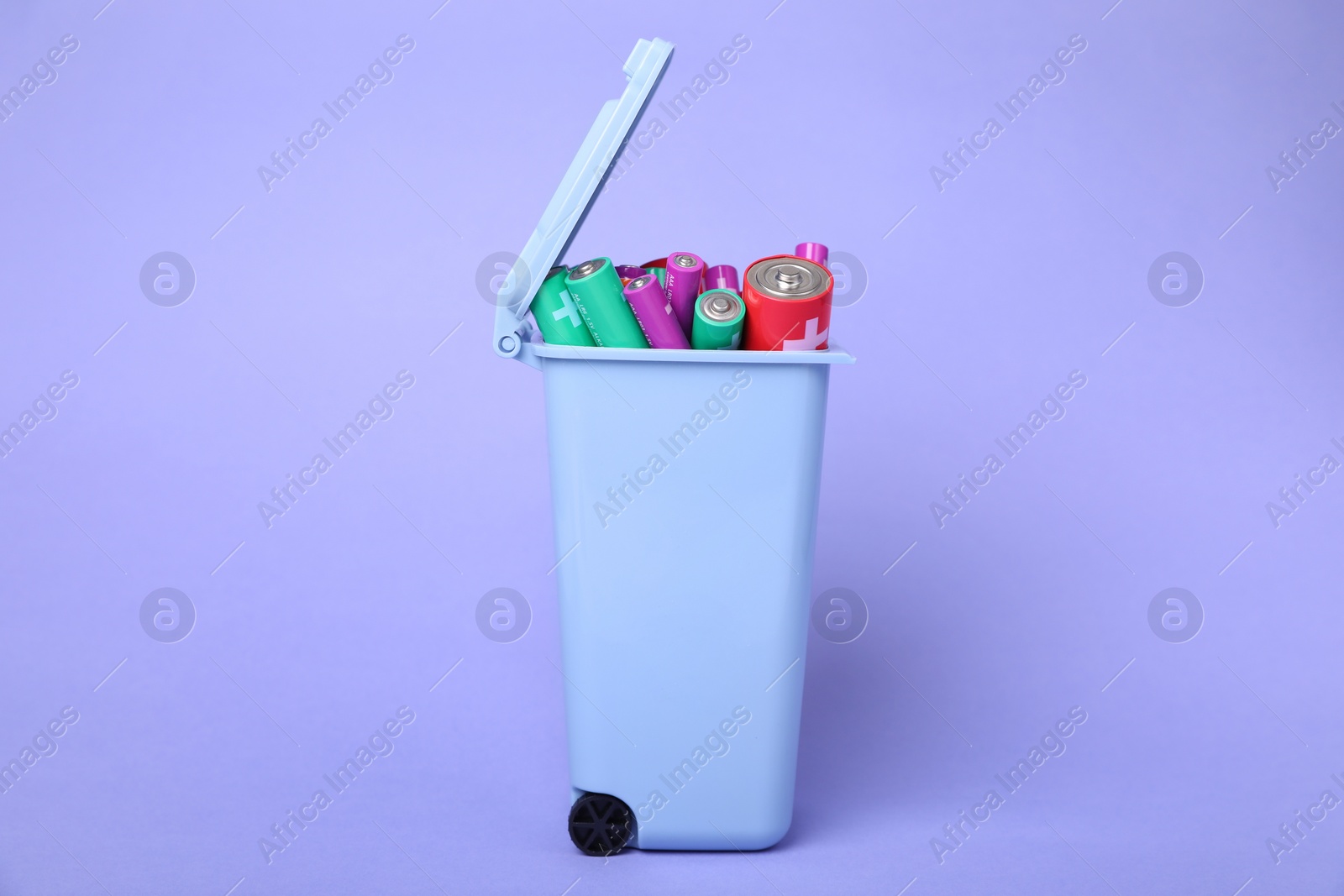 Photo of Many used batteries in recycling bin on light purple background