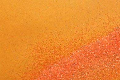 Photo of Shiny bright glitter on orange background, flat lay. Space for text