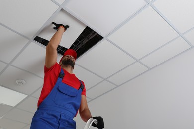 Photo of Electrician repairing ceiling light indoors, low angle view. Space for text