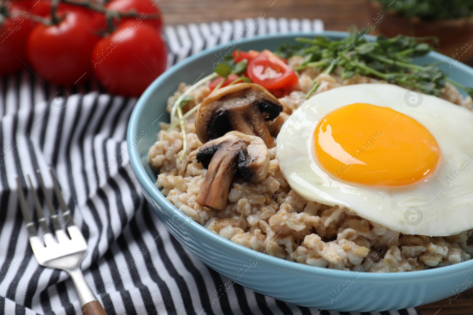 Photo of Tasty boiled oatmeal with fried egg, mushrooms and tomatoes served on table, closeup. Space for text