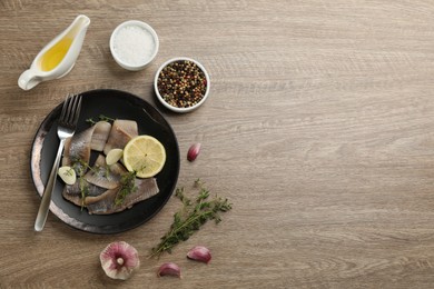 Photo of Delicious salted herring fillets served with lemon, thyme and garlic on wooden table, flat lay. Space for text