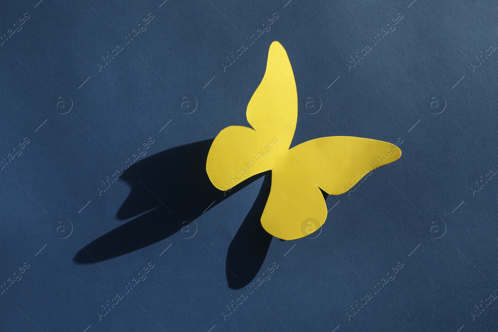 Photo of Yellow paper butterfly on dark blue background, top view