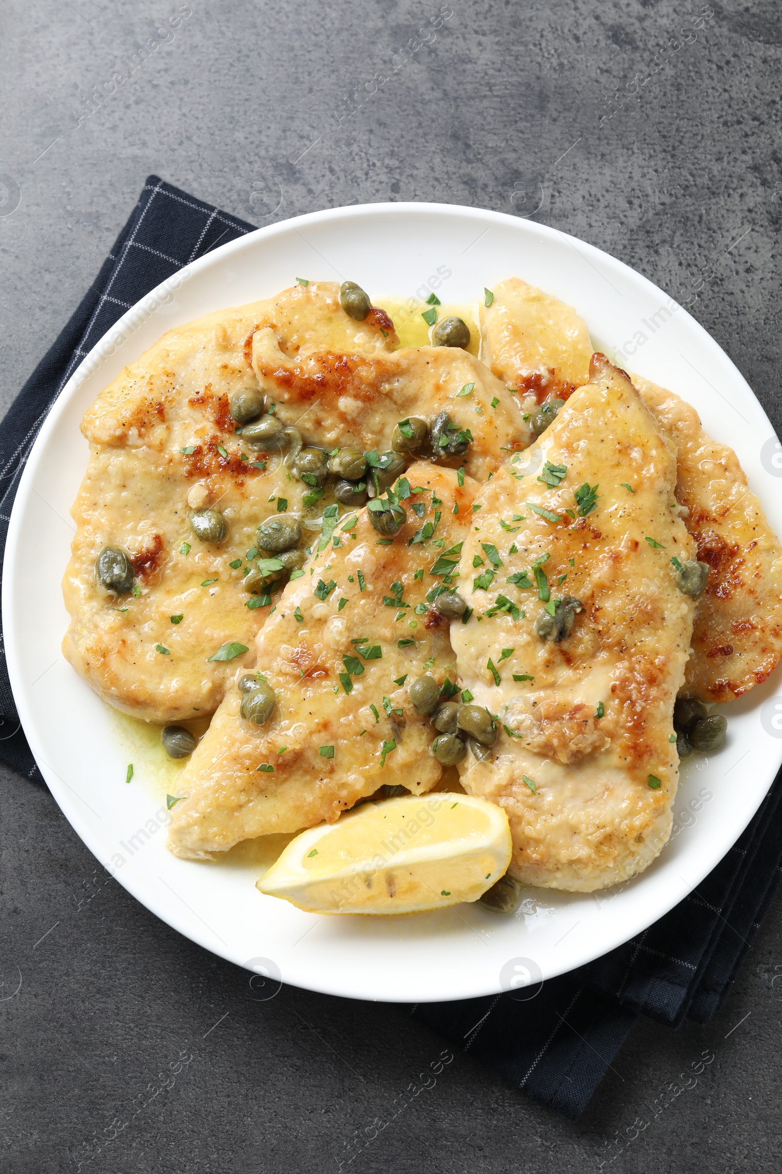 Photo of Delicious chicken piccata with herbs on grey table, top view