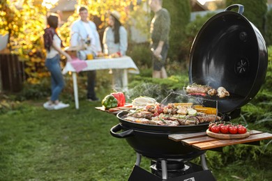 Group of friends having party outdoors. Focus on barbecue grill with food. Space for text