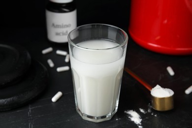 Photo of Amino acid shake, powder, pills and weight plates on black background