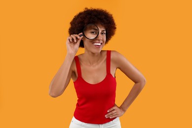 Photo of Smiling woman looking through magnifier glass on orange background