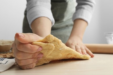 Photo of Woman kneading raw dough at white wooden table, closeup